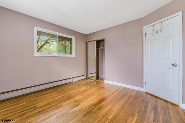 unfurnished bedroom featuring light wood finished floors, a baseboard radiator, a closet, and baseboards