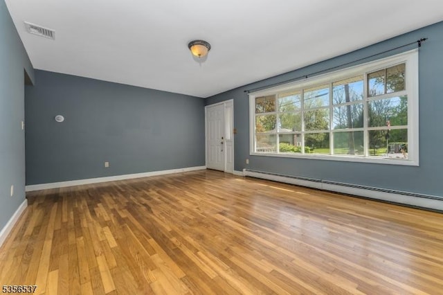 empty room featuring a baseboard heating unit, wood finished floors, and baseboards