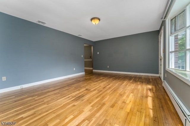 unfurnished room featuring a baseboard heating unit, light wood finished floors, and baseboards