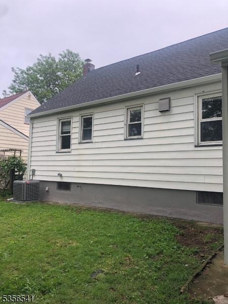 view of side of property featuring central air condition unit, a yard, a chimney, and a shingled roof