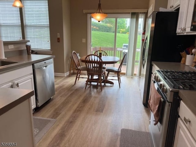 kitchen featuring appliances with stainless steel finishes, white cabinetry, light wood finished floors, hanging light fixtures, and baseboards