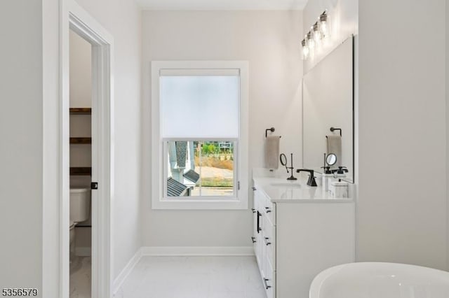 full bath with marble look tiles, vanity, a freestanding bath, and baseboards