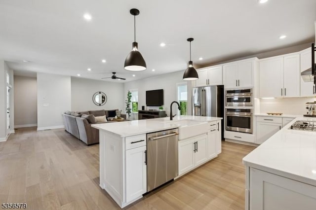 kitchen featuring stainless steel appliances, open floor plan, light countertops, a sink, and recessed lighting