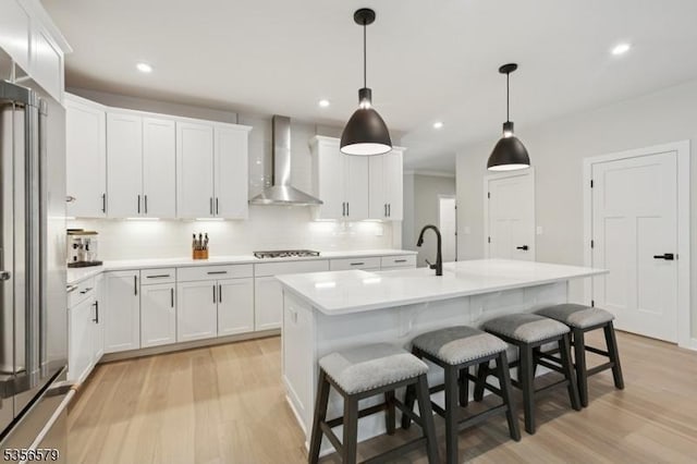 kitchen with wall chimney range hood, high quality fridge, cooktop, a sink, and light wood-style flooring