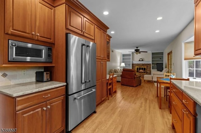 kitchen with appliances with stainless steel finishes, brown cabinets, light wood-style floors, ceiling fan, and open floor plan