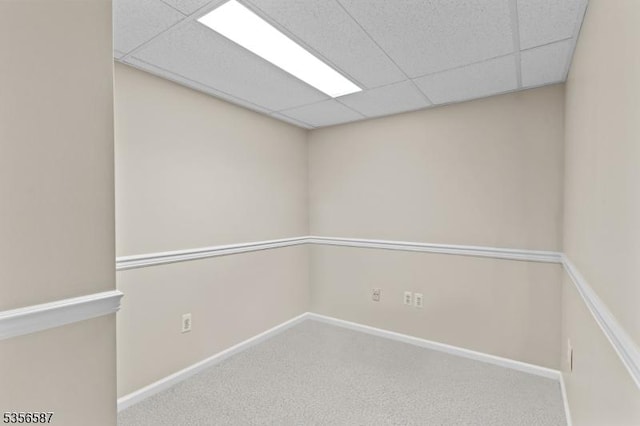 carpeted spare room featuring a drop ceiling and baseboards