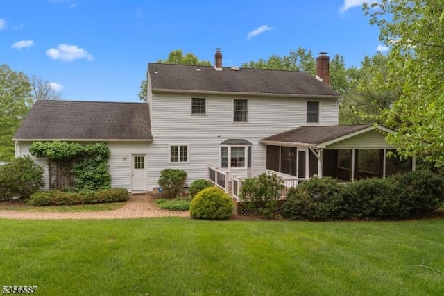 rear view of property with a sunroom, a yard, and a chimney