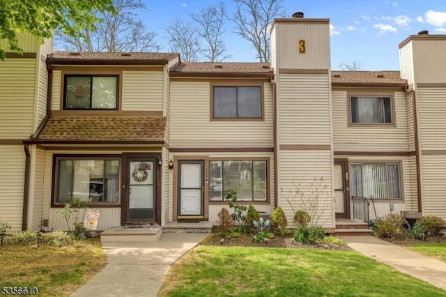 multi unit property featuring roof with shingles, a chimney, and a front lawn