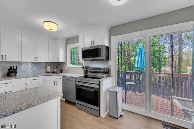 kitchen with appliances with stainless steel finishes, light wood-type flooring, white cabinetry, backsplash, and a sink
