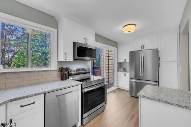 kitchen with stainless steel appliances, backsplash, white cabinets, and light wood-style floors