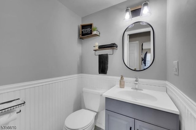 half bath with a wainscoted wall, vanity, and toilet