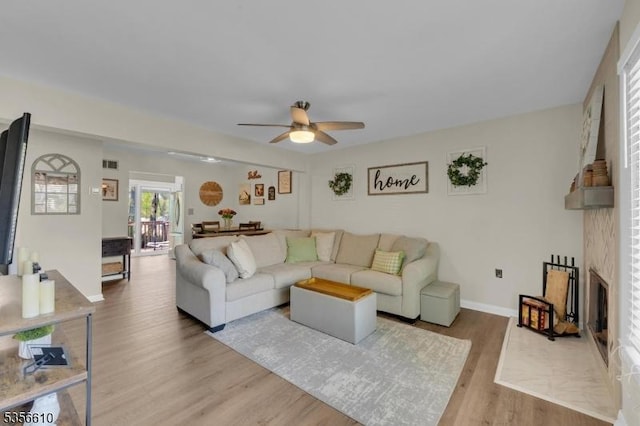 living room with ceiling fan, light wood-style flooring, a fireplace, and baseboards