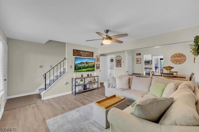 living room with light wood-type flooring, ceiling fan, stairway, and healthy amount of natural light