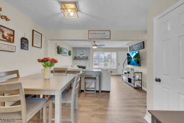 dining area with ceiling fan, light wood-style floors, and a fireplace