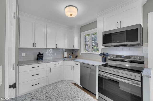 kitchen featuring appliances with stainless steel finishes, a sink, white cabinets, tasteful backsplash, and light stone counters