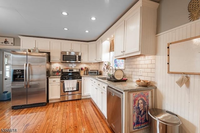 kitchen featuring appliances with stainless steel finishes, a sink, light wood finished floors, white cabinets, and recessed lighting