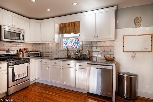 kitchen with stainless steel appliances, white cabinetry, a sink, dark stone countertops, and decorative backsplash