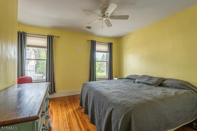 bedroom featuring multiple windows, wood finished floors, baseboards, and a ceiling fan