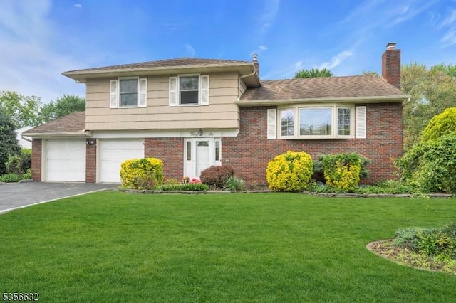 split level home featuring driveway, brick siding, a chimney, a front yard, and a garage