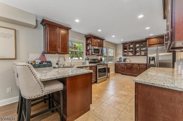 kitchen featuring appliances with stainless steel finishes, a sink, a peninsula, tasteful backsplash, and light stone countertops