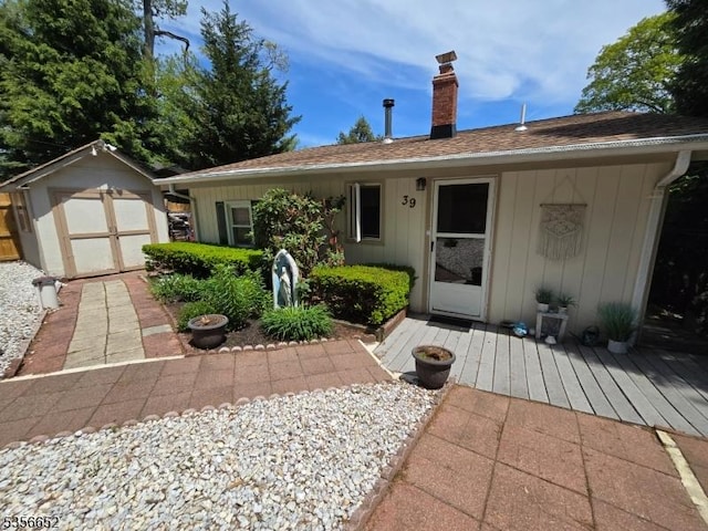 ranch-style home with a chimney, a shed, an outbuilding, and a wooden deck