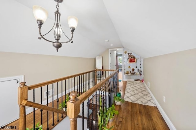 hall with wood finished floors, vaulted ceiling, an upstairs landing, a chandelier, and baseboards