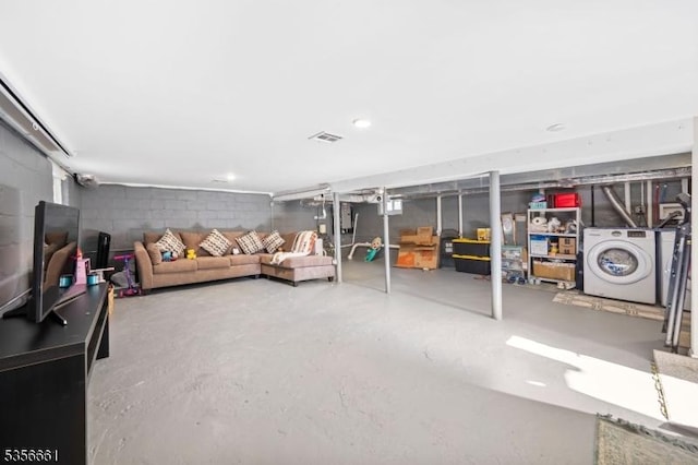 living area featuring washer / dryer, concrete block wall, and concrete floors