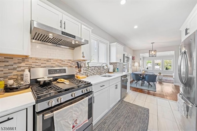 kitchen with stainless steel appliances, under cabinet range hood, a sink, white cabinetry, and light countertops