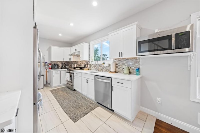 kitchen featuring appliances with stainless steel finishes, under cabinet range hood, tasteful backsplash, light countertops, and white cabinetry