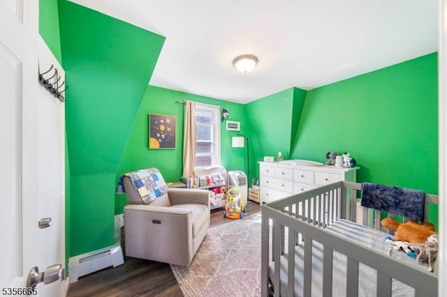 bedroom with a baseboard heating unit, dark wood-style flooring, and a nursery area