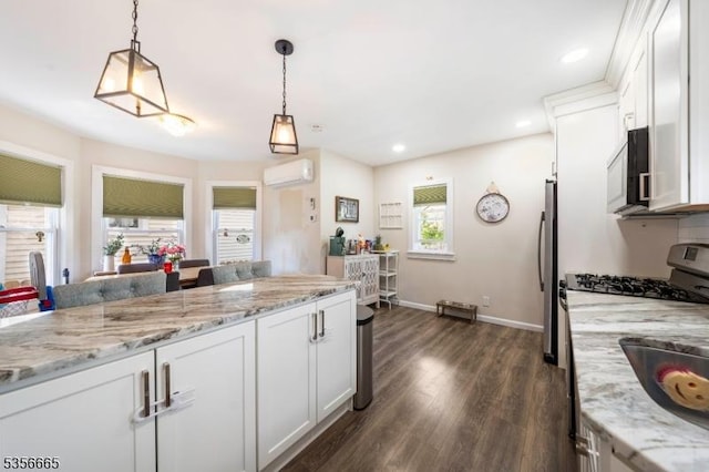 kitchen featuring stainless steel appliances, an AC wall unit, dark wood-style floors, white cabinets, and decorative light fixtures