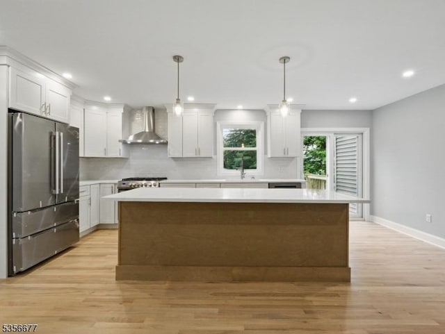 kitchen with appliances with stainless steel finishes, wall chimney range hood, light wood finished floors, a sink, and light countertops