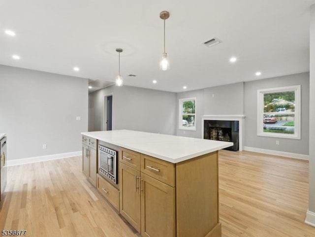 kitchen with stainless steel microwave, light wood-style flooring, a center island, decorative light fixtures, and baseboards