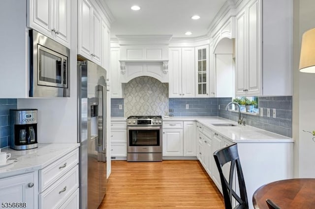 kitchen featuring stainless steel appliances, a sink, white cabinetry, tasteful backsplash, and light wood-style floors