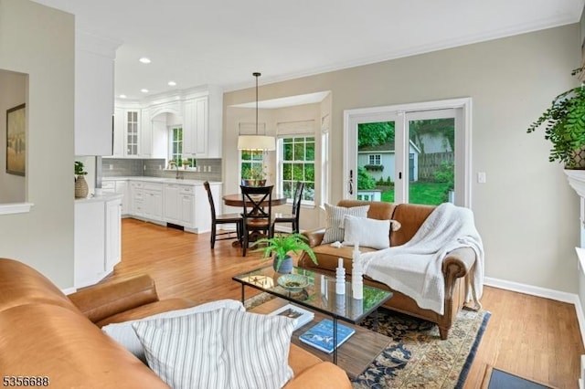 living room featuring light wood-style flooring, crown molding, baseboards, and recessed lighting