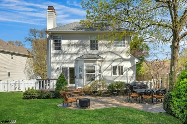 rear view of property with a chimney, a patio area, a fire pit, roof with shingles, and a deck