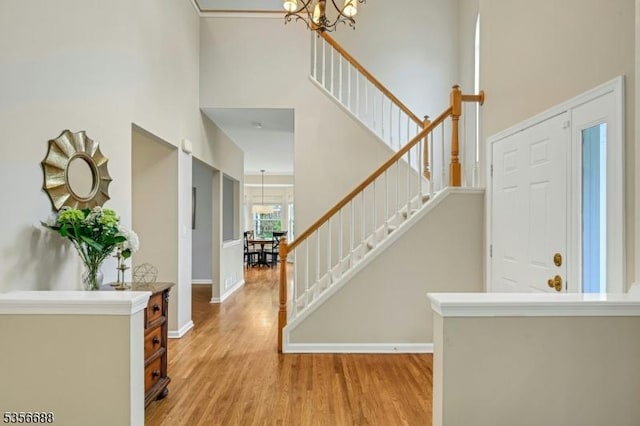 foyer entrance with a chandelier, stairway, light wood-type flooring, a towering ceiling, and baseboards
