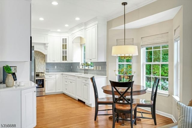 kitchen featuring gas range, light countertops, tasteful backsplash, white cabinetry, and light wood finished floors