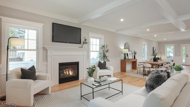 living room featuring beamed ceiling, light wood finished floors, plenty of natural light, a glass covered fireplace, and recessed lighting
