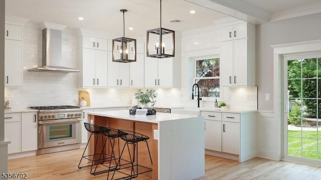 kitchen featuring wall chimney range hood, high end stainless steel range oven, a sink, light wood-style flooring, and ornamental molding