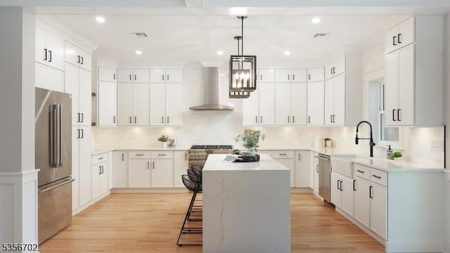 kitchen featuring high quality appliances, wall chimney exhaust hood, a kitchen island, decorative backsplash, and a sink