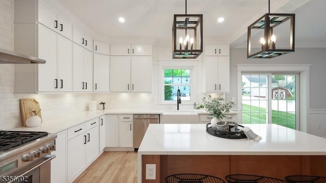 kitchen featuring stainless steel appliances, wall chimney exhaust hood, a sink, light countertops, and recessed lighting
