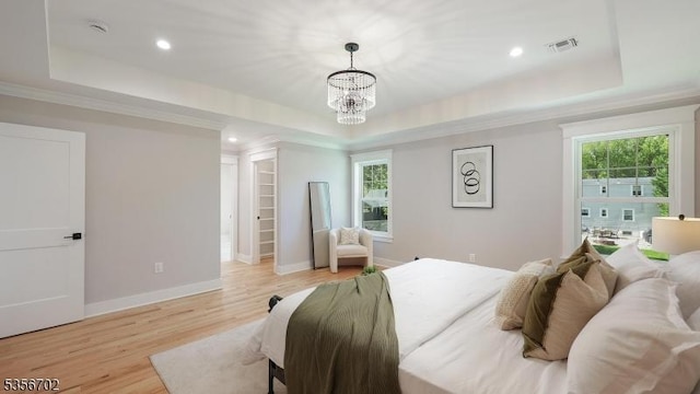 bedroom with a tray ceiling, a chandelier, light wood finished floors, a spacious closet, and ornamental molding