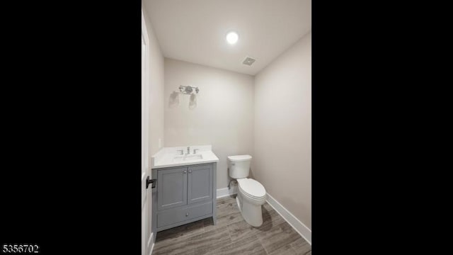 half bath featuring toilet, vanity, baseboards, and wood finished floors