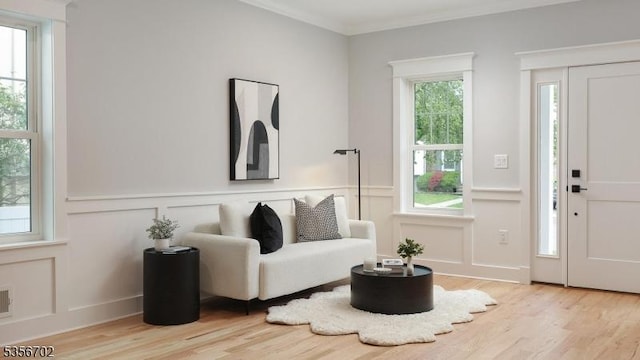 sitting room featuring a decorative wall, wood finished floors, crown molding, and a wainscoted wall