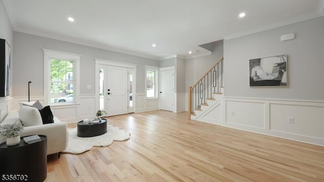 living area featuring a decorative wall, stairs, light wood-style flooring, crown molding, and wainscoting