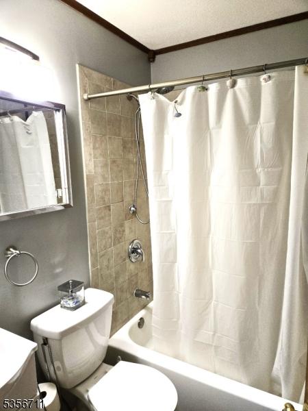 bathroom with crown molding, shower / bathtub combination with curtain, toilet, and vanity