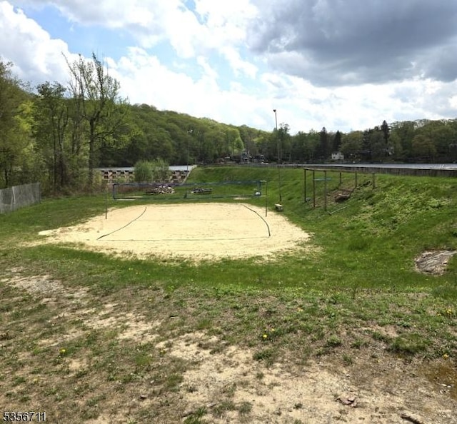 surrounding community with fence, a wooded view, volleyball court, and a view of countryside