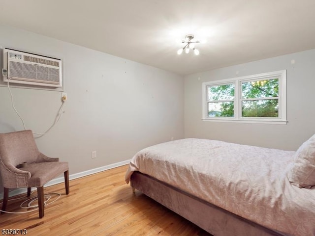 bedroom featuring a wall mounted AC, light wood-style flooring, baseboards, and a chandelier