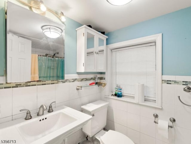 bathroom with tile walls, a sink, curtained shower, and toilet